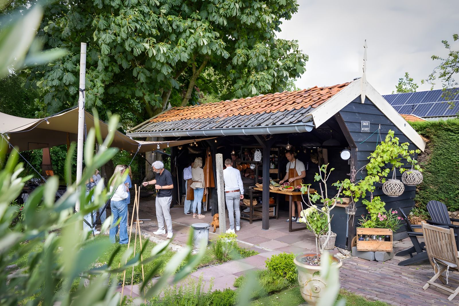 De stretchtent met de buitenkeuken in de tuin, gasten aan het koken